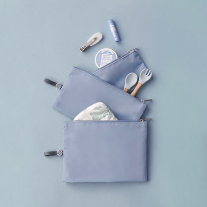 Set of 3 blue packing pouches in varying sizes, laid flat and packed with baby items like diapers, utensils, and hair clips.