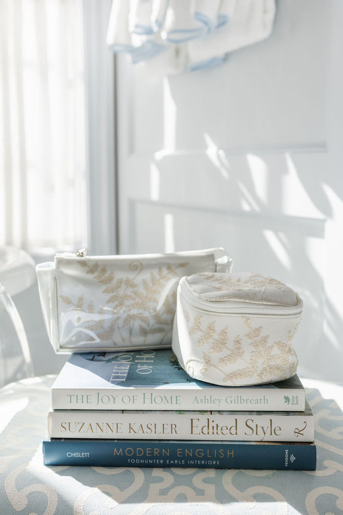 Fern travel cases displayed on books beside a window by Lenora