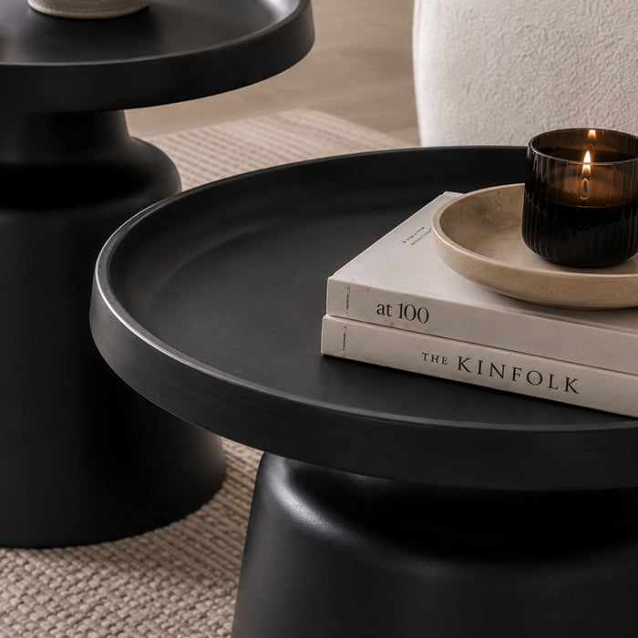 Close-up of the Gallery Everyday Minerva Coffee Table - Black Set of 2, showing a matte black pedestal table styled with books, a candle, and matching table in the background.