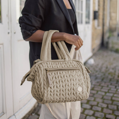 Paige Mini Beige carried by the handles, showing the herringbone quilting and gold hardware details.